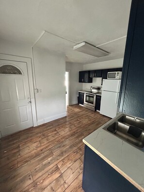 A kitchen with wooden flooring, a white refrigerator, a microwave, and a stainless steel sink.