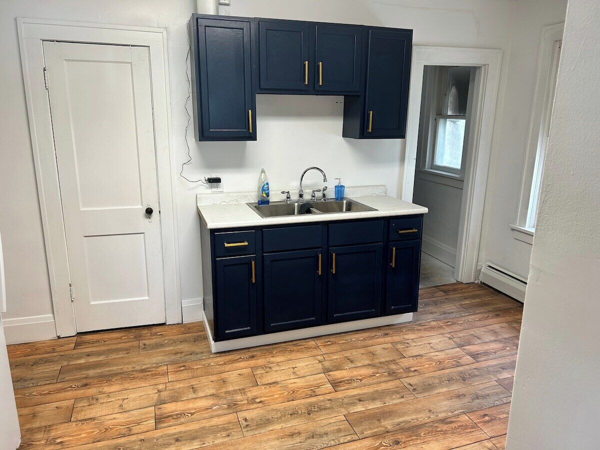 A kitchen with dark cabinets, a white countertop, and a wooden floor.