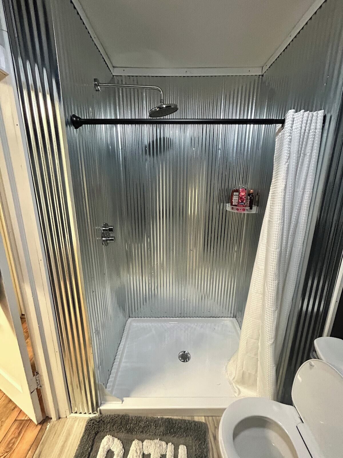A compact bathroom with a shower, toilet, and a small shelf with toiletries.