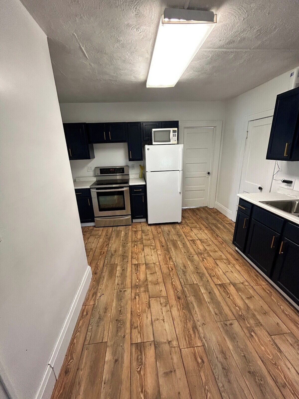 A compact kitchen with dark cabinets, a white refrigerator, and a microwave on top.