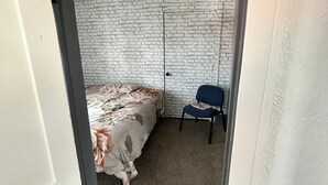 A bedroom with a bed, a chair, a white brick wall, and a door.