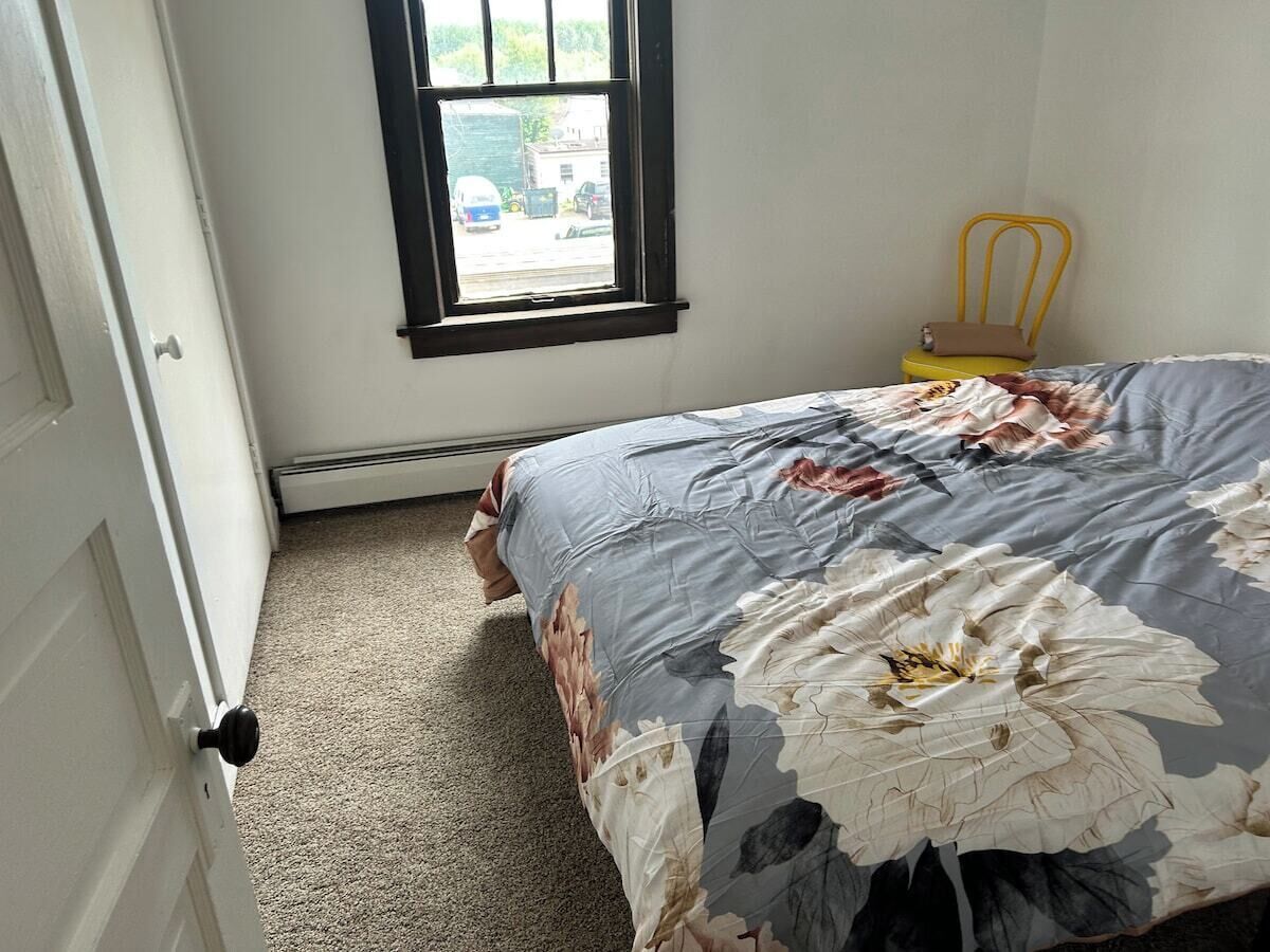 A bedroom with a bed, a window, a chair, and a door.