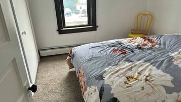 A bedroom with a bed, a window, a chair, and a door.