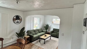 A living room with a wooden floor, a green sofa, a coffee table, and a dining table with chairs.