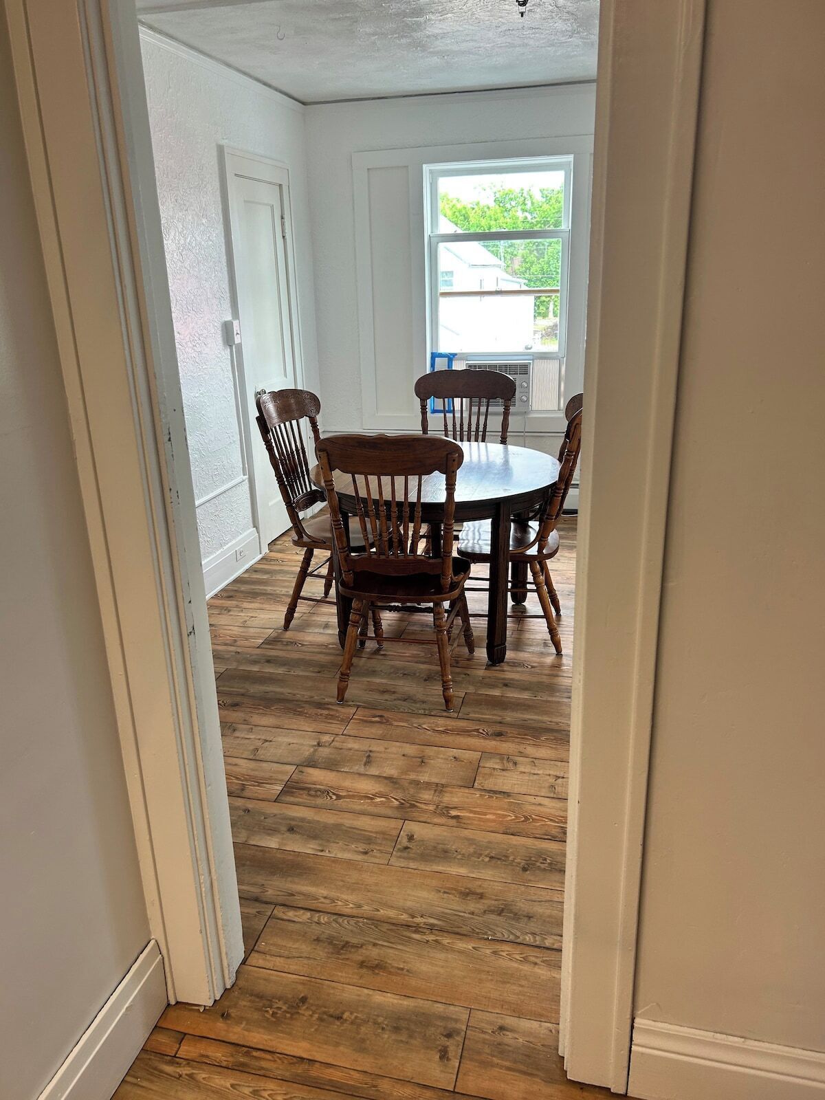 A dining area with a round table and four chairs, wooden flooring, and white walls.