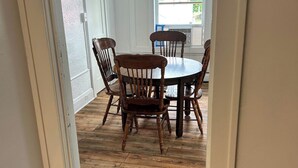 A dining area with a round table and four chairs, wooden flooring, and white walls.