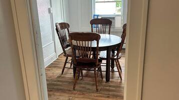 A dining area with a round table and four chairs, wooden flooring, and white walls.