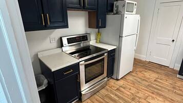 A kitchen with dark cabinets, a stainless steel oven, a microwave, and a white refrigerator.