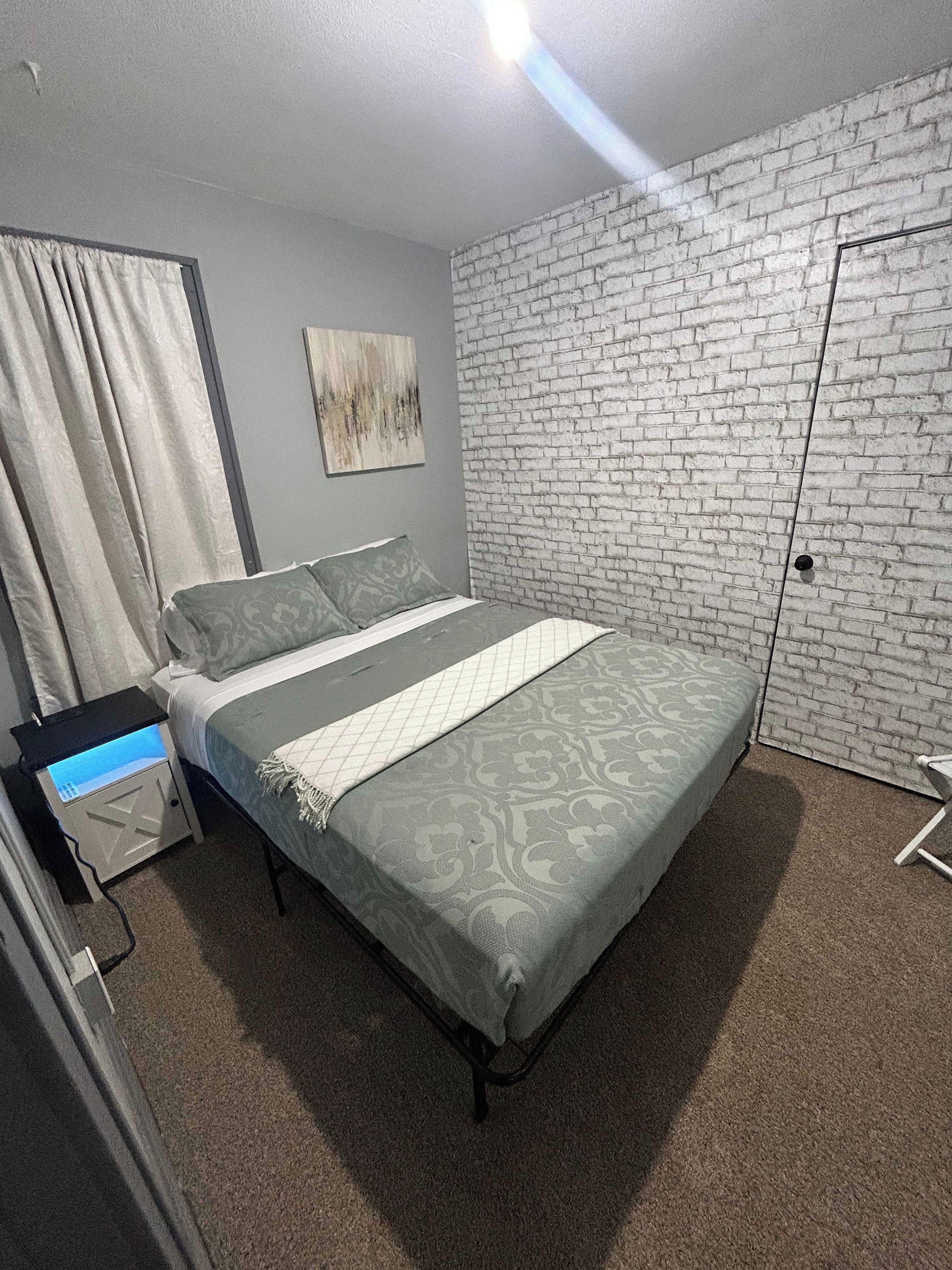 Un dormitorio con una cama, una mesita de noche, una pared con diseño de ladrillo y una puerta.