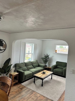 A living room with a green sofa, a wooden coffee table, and a potted plant. - Bright Modern Bath & Cozy Living Oasis (Mountain Iron)