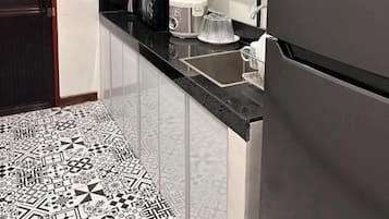 A compact kitchen with a refrigerator, a microwave, a coffee maker, and a sink.