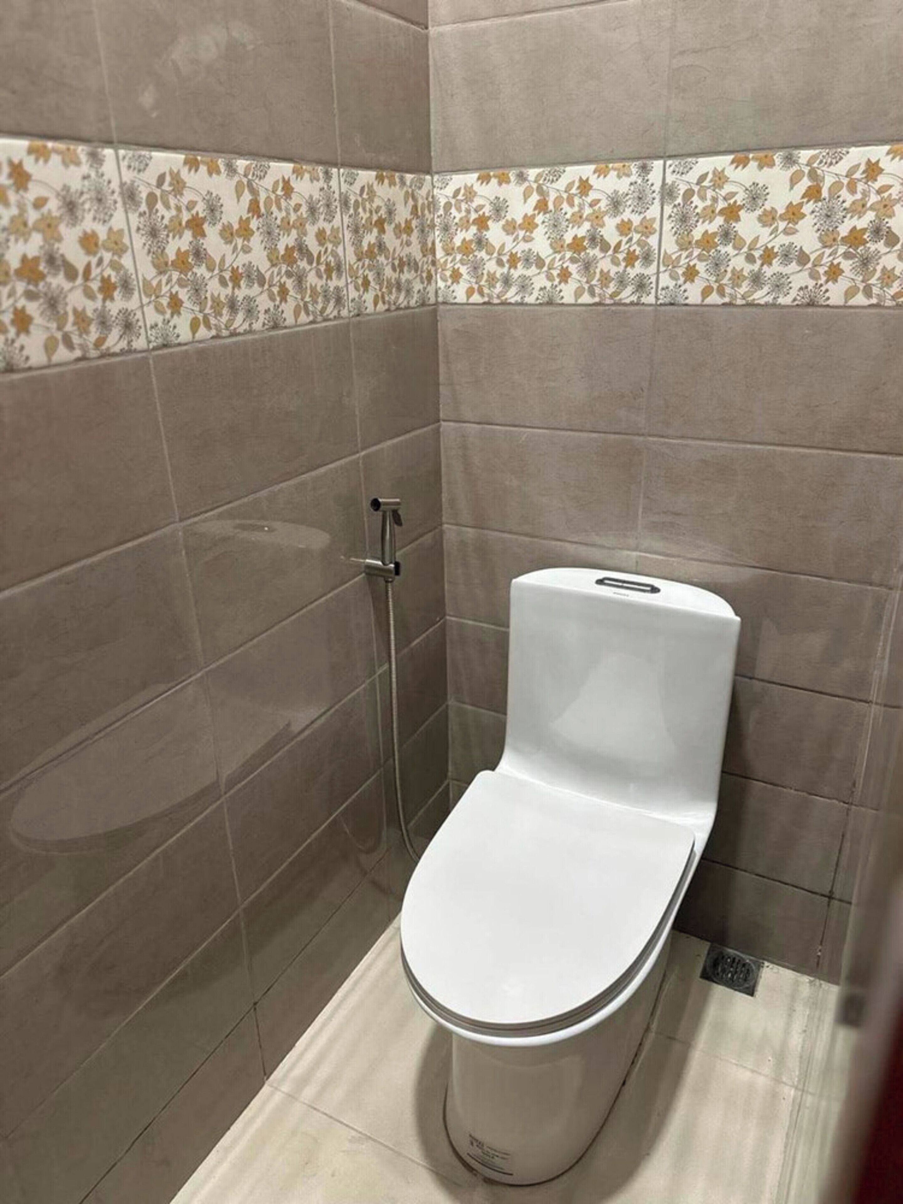 Een badkamer met toilet, douche en een betegelde muur met een bloemenmotief.