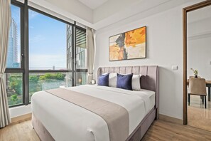 A modern bedroom with a large bed, a view of greenery and buildings, and a painting on the wall. - Weska by Kozystay - Cilandak (South Jakarta)