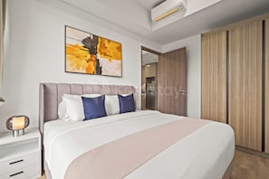 A modern bedroom with a large bed, a nightstand, a bedside lamp, a painting on the wall, and a wardrobe. - Weska by Kozystay - Cilandak (South Jakarta)
