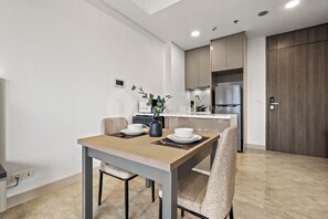A modern dining area with a wooden table and chairs, a kitchen in the background, and a wooden door. - Weska by Kozystay - Cilandak (South Jakarta)