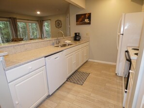 A kitchen with white cabinets, a dishwasher, a coffee maker, and a refrigerator. - Whispering Creek at Pinebrook (Bellaire)