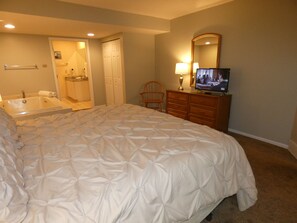 Ein Schlafzimmer mit einem großen Bett, einem Fernseher, einem Schminktisch und einem durch eine offene Tür einsehbaren Badezimmer.