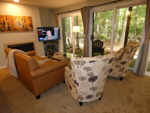 A living room with a sofa, armchair, television, and a glass door leading to a patio. - Whispering Creek at Pinebrook (Bellaire)