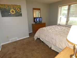 A bedroom with a bed, a dresser, a television, and a window with blinds. - Whispering Creek at Pinebrook (Bellaire)