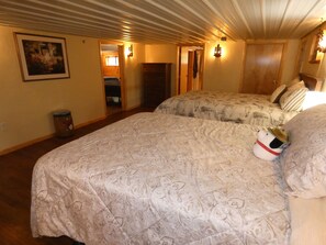Quarto de hotel com duas camas, piso de madeira, quadro na parede e lixeira.