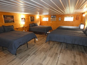 A cabin with three beds, wooden walls, and a sloped ceiling. - Woodland Hangout.  Gather. Play. Explore. (Mancelona)
