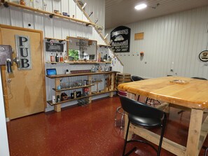 A pub interior with a wooden bar, shelves with bottles, a wooden door labeled 'PUB', and a sign for 'DOUG'S GARAGE'.