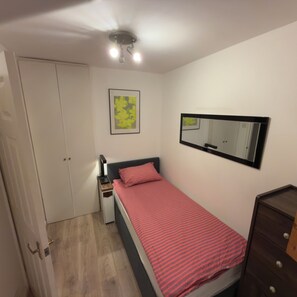 A bedroom with a bed, a dresser, a nightstand, a mirror, and a door. - Cosy City Apartment (London)