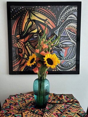 A framed abstract painting with a vase of sunflowers on a table with a colorful patterned tablecloth. - Cosy City Apartment (London)