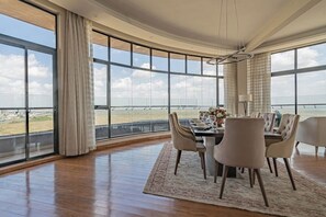 A dining area with a large table, chairs, and a view of the sea through expansive windows. - Luxurious  2BR Penthouse, breathtaking views of  National park Nairobi. (Nairobi)