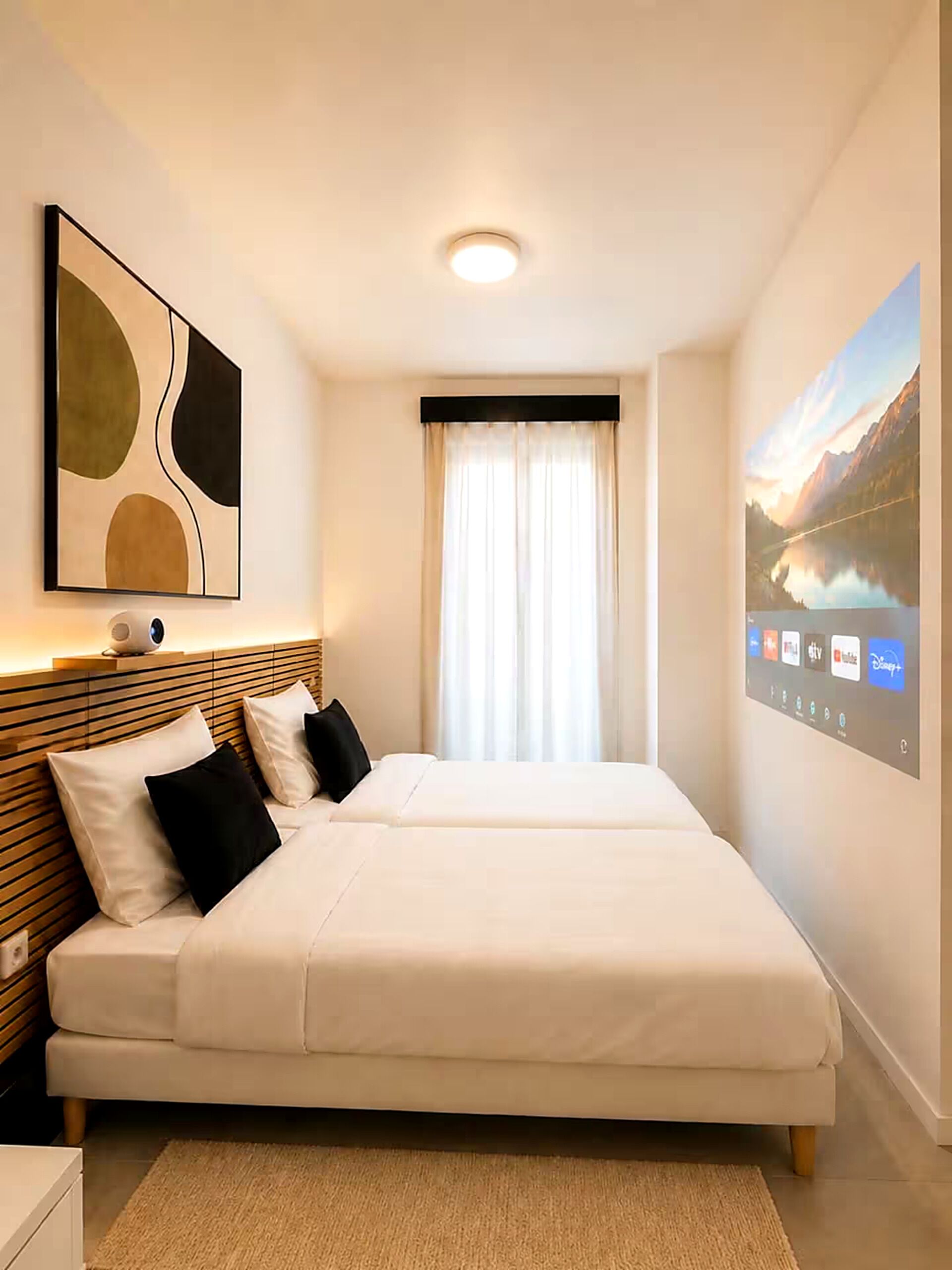 A hotel room with a large bed, a bedside table, a wall-mounted TV, and a window with curtains.