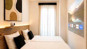 A hotel room with a large bed, a bedside table, a wall-mounted TV, and a window with curtains.