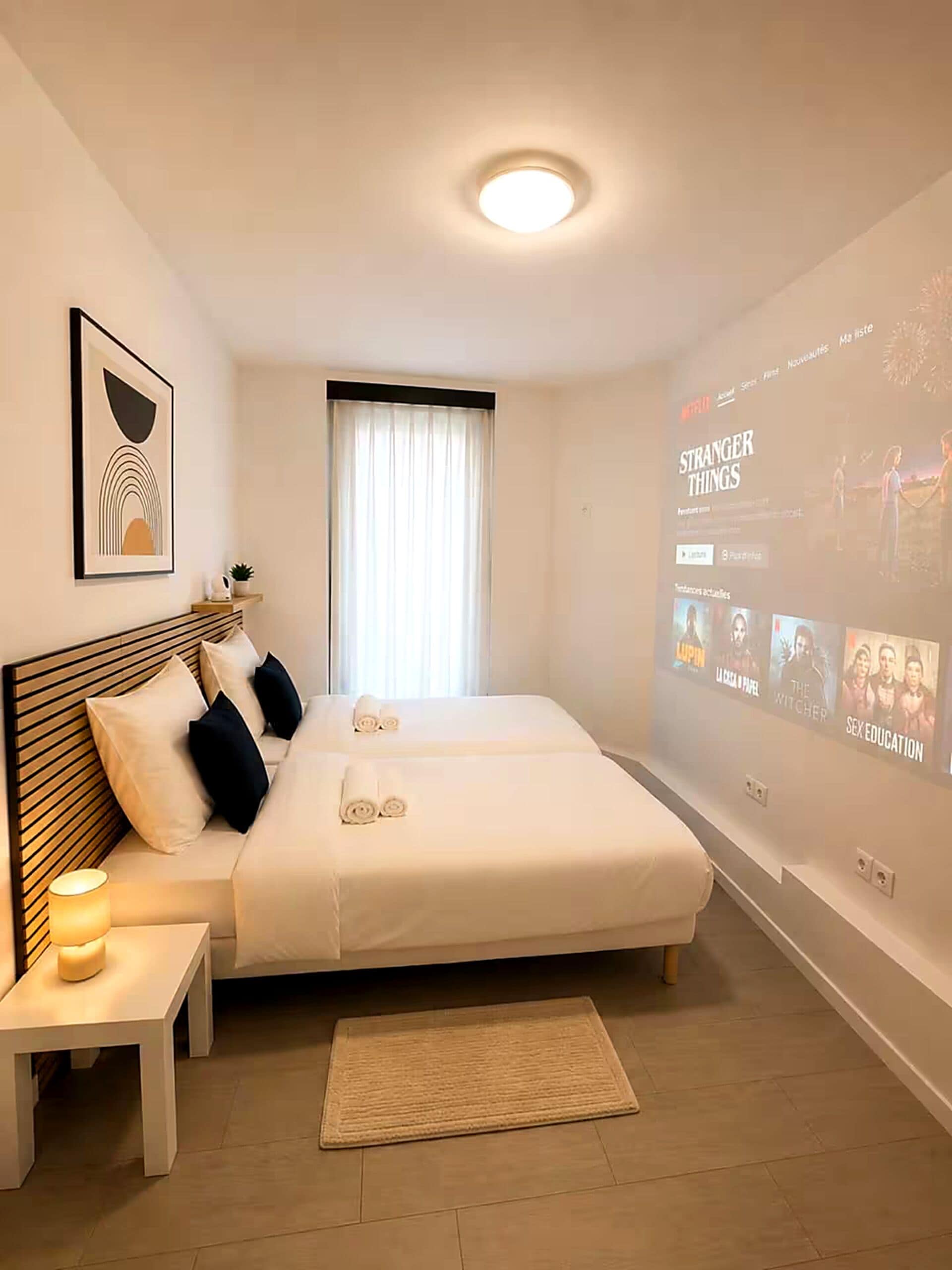 Une chambre d’hôtel équipée d’un lit, d’une table de chevet et d’un projecteur fixé au mur, qui diffuse un film.