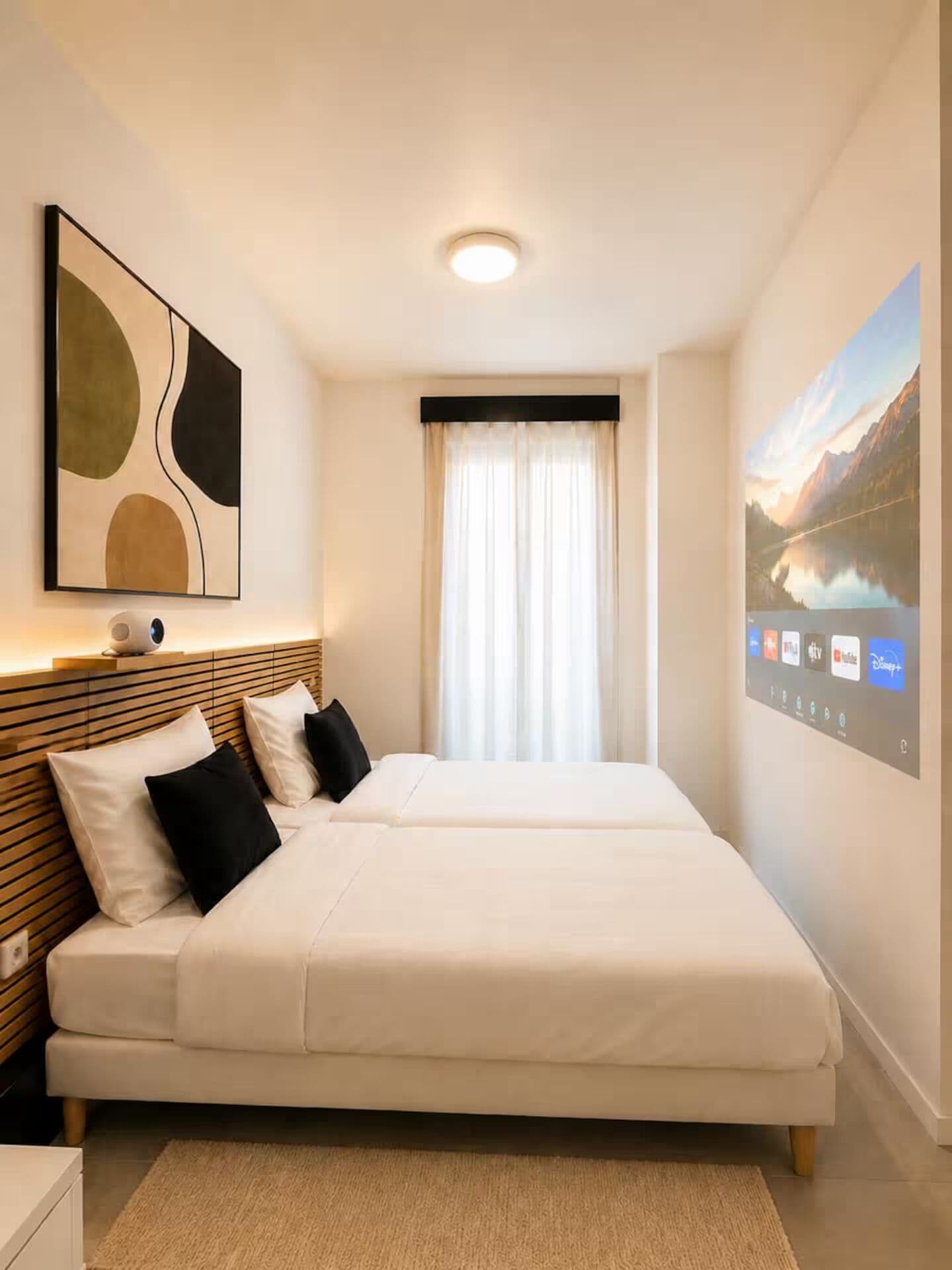 A hotel room with a bed, a wall-mounted TV, and a painting.