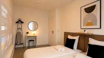 Een hotelkamer met twee bedden, een bureau met stoel, een spiegel en een lijst met een foto aan de muur.