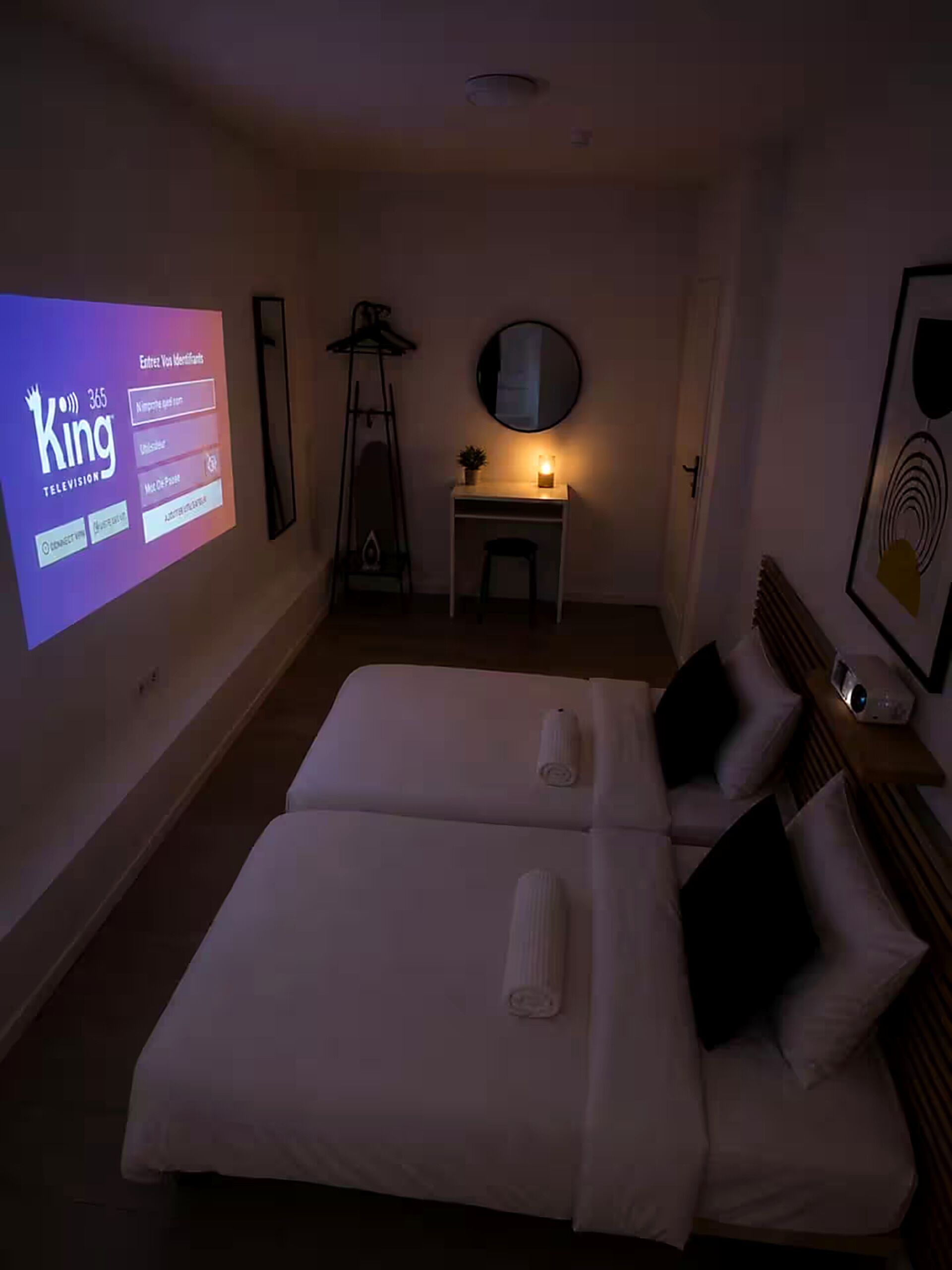 Een hotelkamer met een bed, nachtkastje, lamp en een aan de muur bevestigde televisie waarop een zenderoverzicht wordt weergegeven.