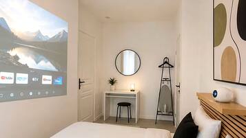 Une chambre à coucher comprenant un lit, un bureau, une chaise, un miroir et un écran de projection sur lequel est diffusé un paysage pittoresque.