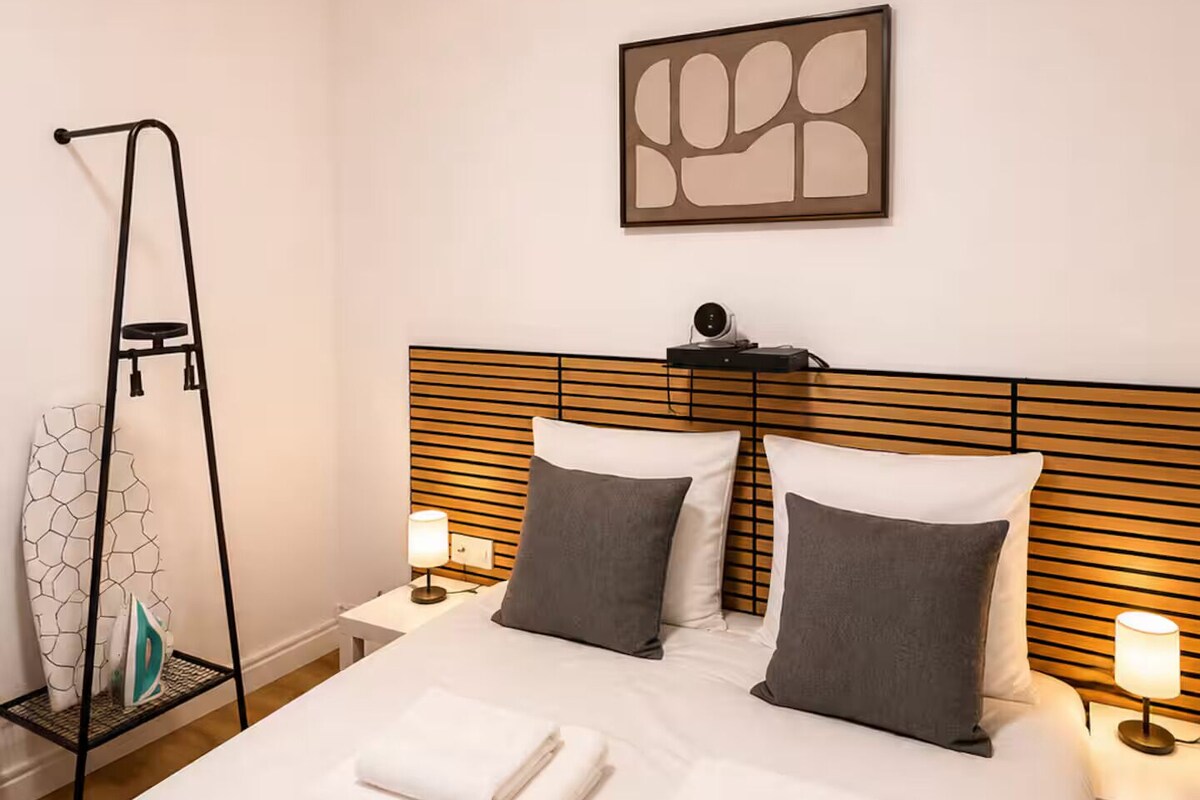 A hotel room with a bed, two bedside tables, a wall-mounted artwork, and a towel rack.