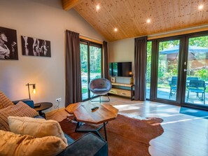 Een moderne woonkamer met een bank, een houten salontafel, een televisie en een groot raam met gordijnen.
