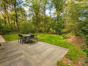 Een terras met een tafel en stoelen, omringd door een gazon en bomen.