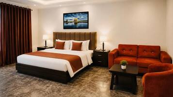 A hotel room with a large bed, a sofa, a small table, and a painting on the wall.
