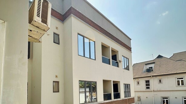 A multi-story residential building with balconies, a car parked in the driveway, and an air conditioning unit on the exterior wall. - Swan Luxury Homes (Abuja)
