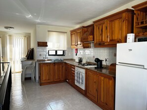 A kitchen with wooden cabinets, a white refrigerator, and a window with blinds. - Charming 3-Bedroom Apartment with 3 Terraces (San Pawl il-Baħar)