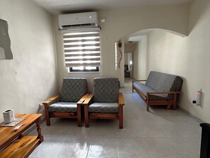 A living room with two armchairs, a sofa, a wooden table, and an air conditioning unit. - Charming 3-Bedroom Apartment with 3 Terraces (San Pawl il-Baħar)