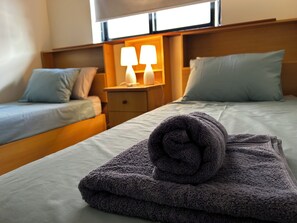 A hotel room with two beds, a nightstand with lamps, and a rolled towel on the bed. - Charming 3-Bedroom Apartment with 3 Terraces (San Pawl il-Baħar)