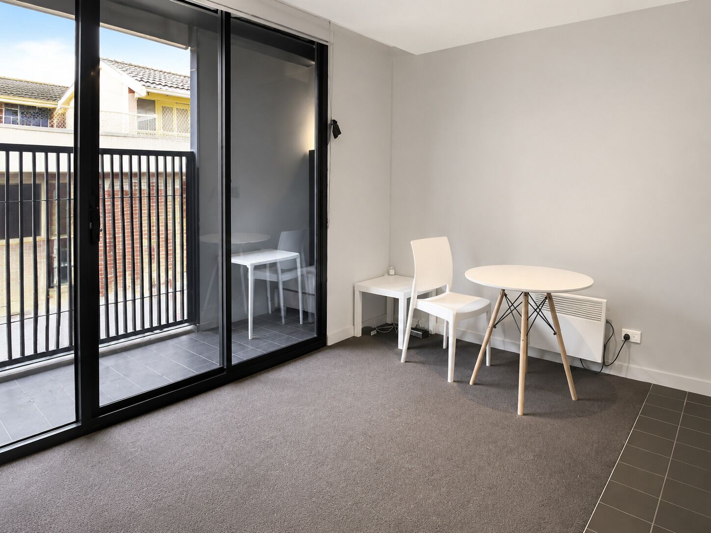 A room with a sliding glass door leading to a balcony, a small round table with two chairs, and a radiator on the wall.