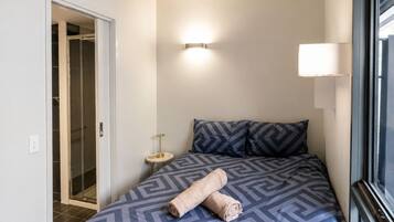 A hotel room with a bed, a bedside lamp, a small table, and a window.