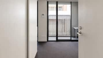 A hallway leading to a balcony with a metal railing, a small table, and a door with a handle.