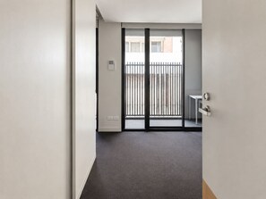A hallway leading to a balcony with a metal railing, a small table, and a door with a handle. - Stylish Modern Studio - A Sweet Escape for Two (Box Hill)