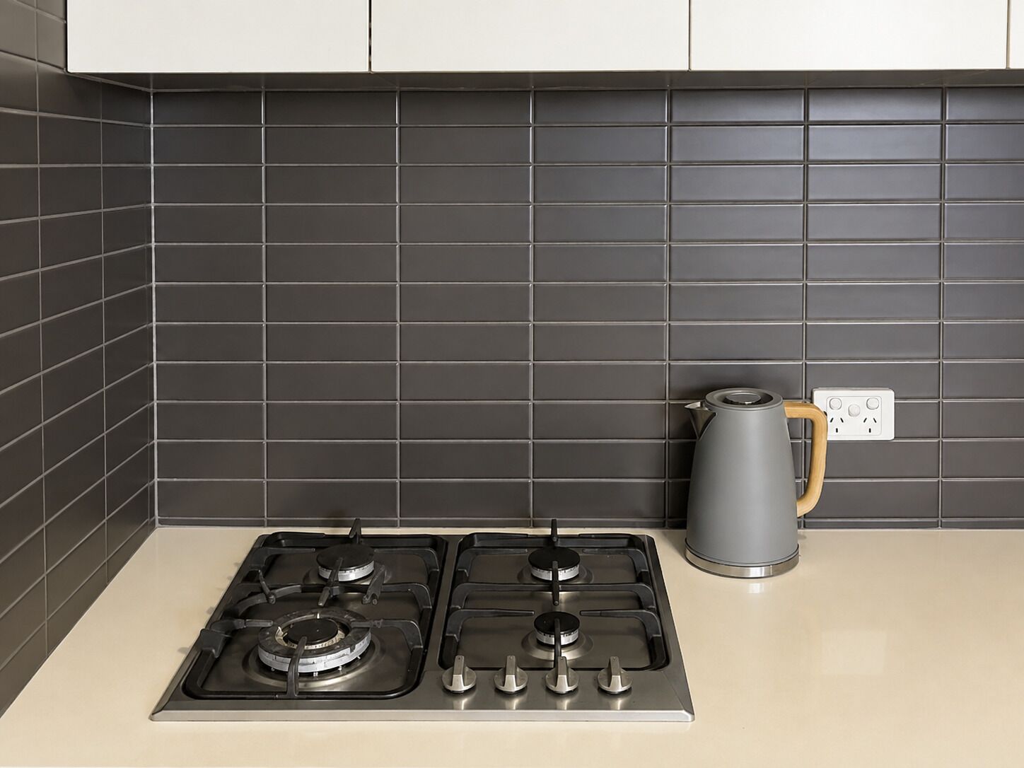 A kitchen with two gas stoves, a kettle, and a power outlet on the countertop.
