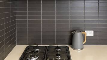 A kitchen with two gas stoves, a kettle, and a power outlet on the countertop.